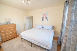 A bedroom with a bed, a wooden dresser, a lamp, and a door.
