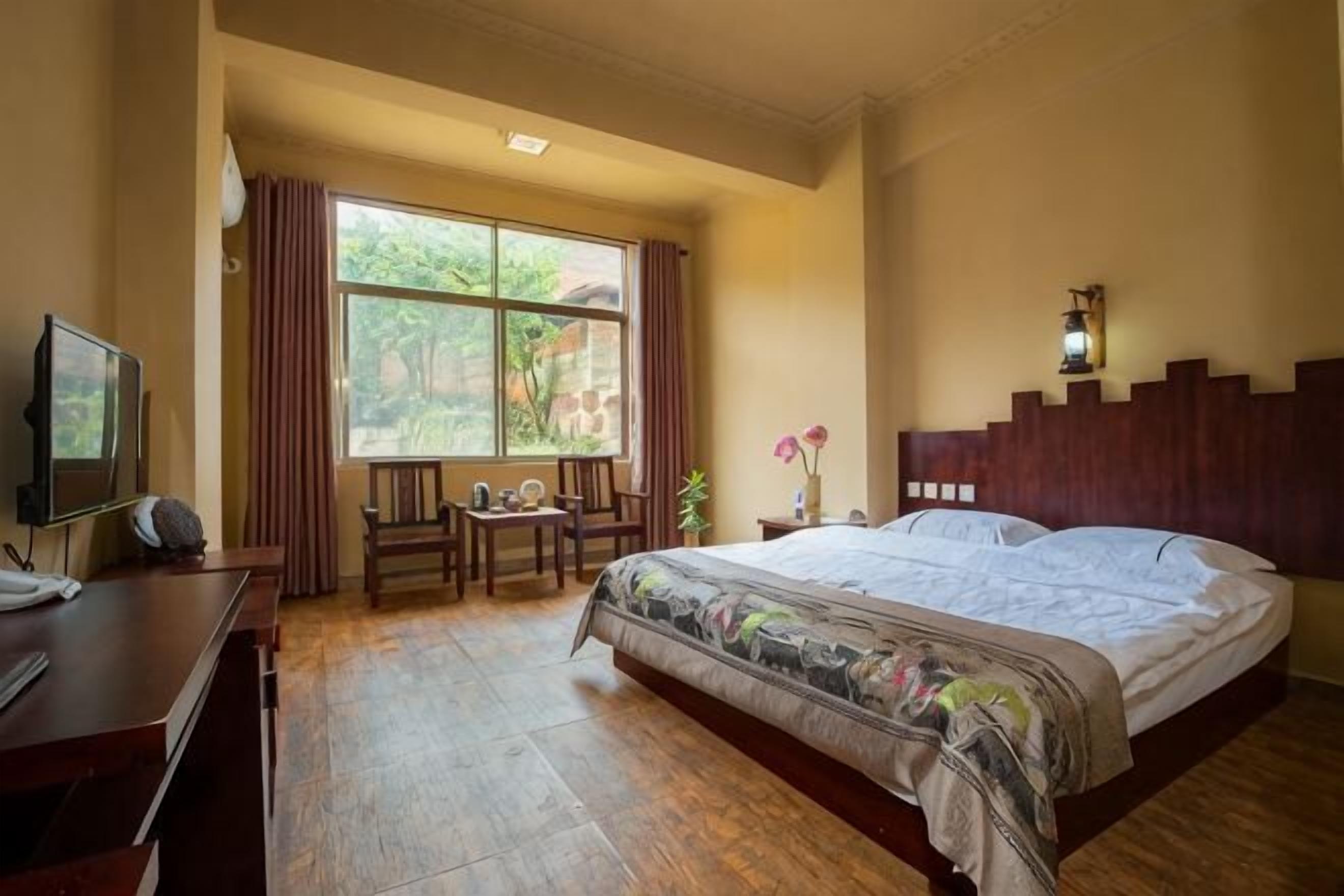 A bedroom with a bed, a desk, a chair, a TV, and a window with curtains.