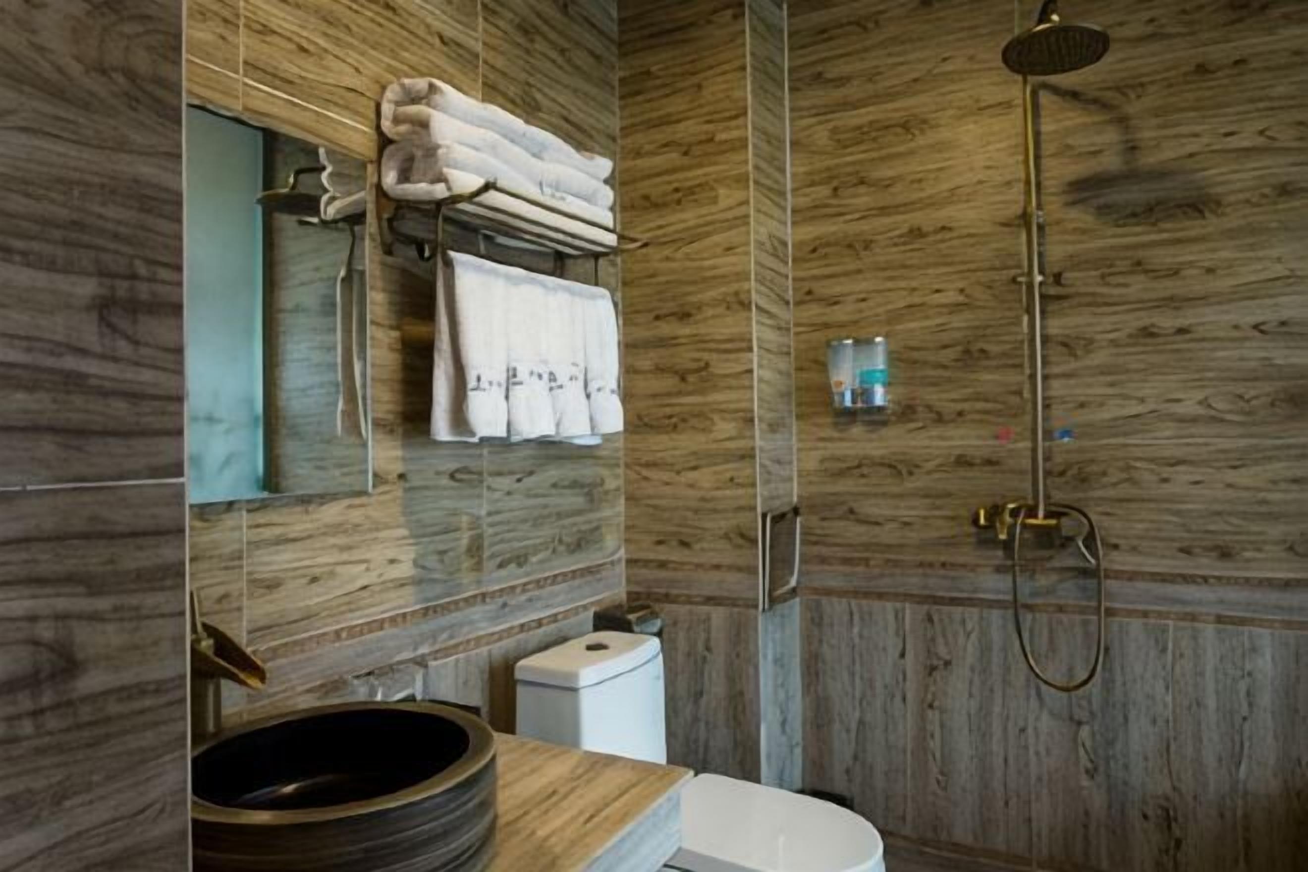 Un baño con pared de madera, un lavamanos redondo, un inodoro y una ducha.