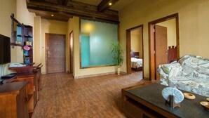 Una habitación con piso de madera, un sofá, un televisor, un escritorio y una planta.