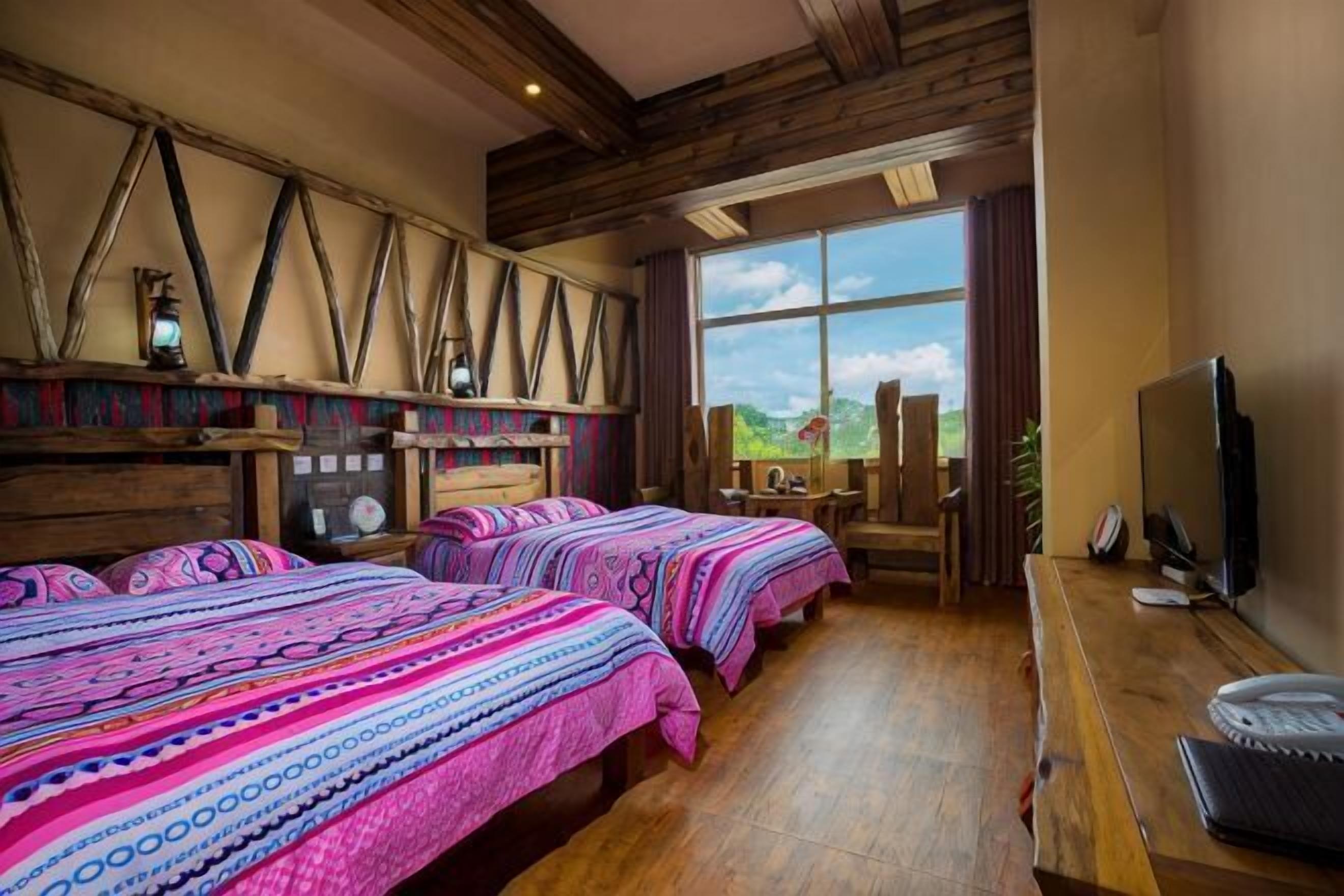 Una habitación con tres camas, un escritorio de madera, una televisión y un ventanal con vistas al exterior.