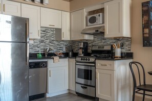 A compact kitchen with white cabinets, a stainless steel refrigerator, a microwave, a stove, and a coffee maker.