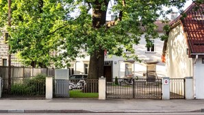 A gated residential area with a tree, a white building, and a parked motorcycle. - Vintage Apartments Blue / Free parking (Rīga)