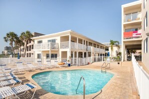 Un espace piscine avec des chaises longues et un bâtiment doté de balcons.