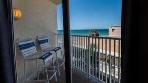 Een balkon met twee witte stoelen en een kleine tafel, met uitzicht op een strand en een gebouw.