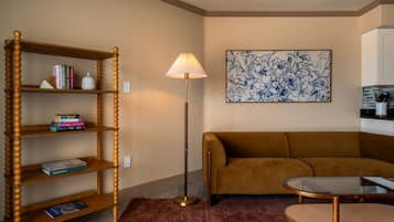 A living room with a wooden bookshelf, a brown sofa, a round coffee table, a floor lamp, and a floral artwork on the wall.