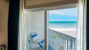 Un balcon donnant sur une plage, avec des chaises blanches et une balustrade.