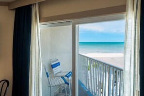 Un balcon donnant sur une plage, avec des chaises blanches et une balustrade.