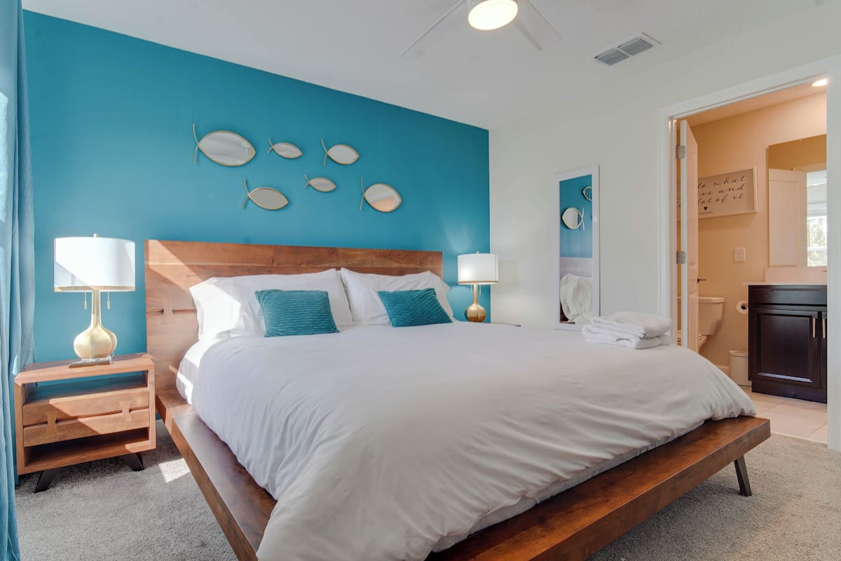 A bedroom with a large bed, two bedside tables with lamps, a wooden headboard, and a blue accent wall.