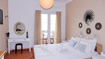 A bedroom with a bed, a desk, a chair, a mirror, and a balcony with curtains.