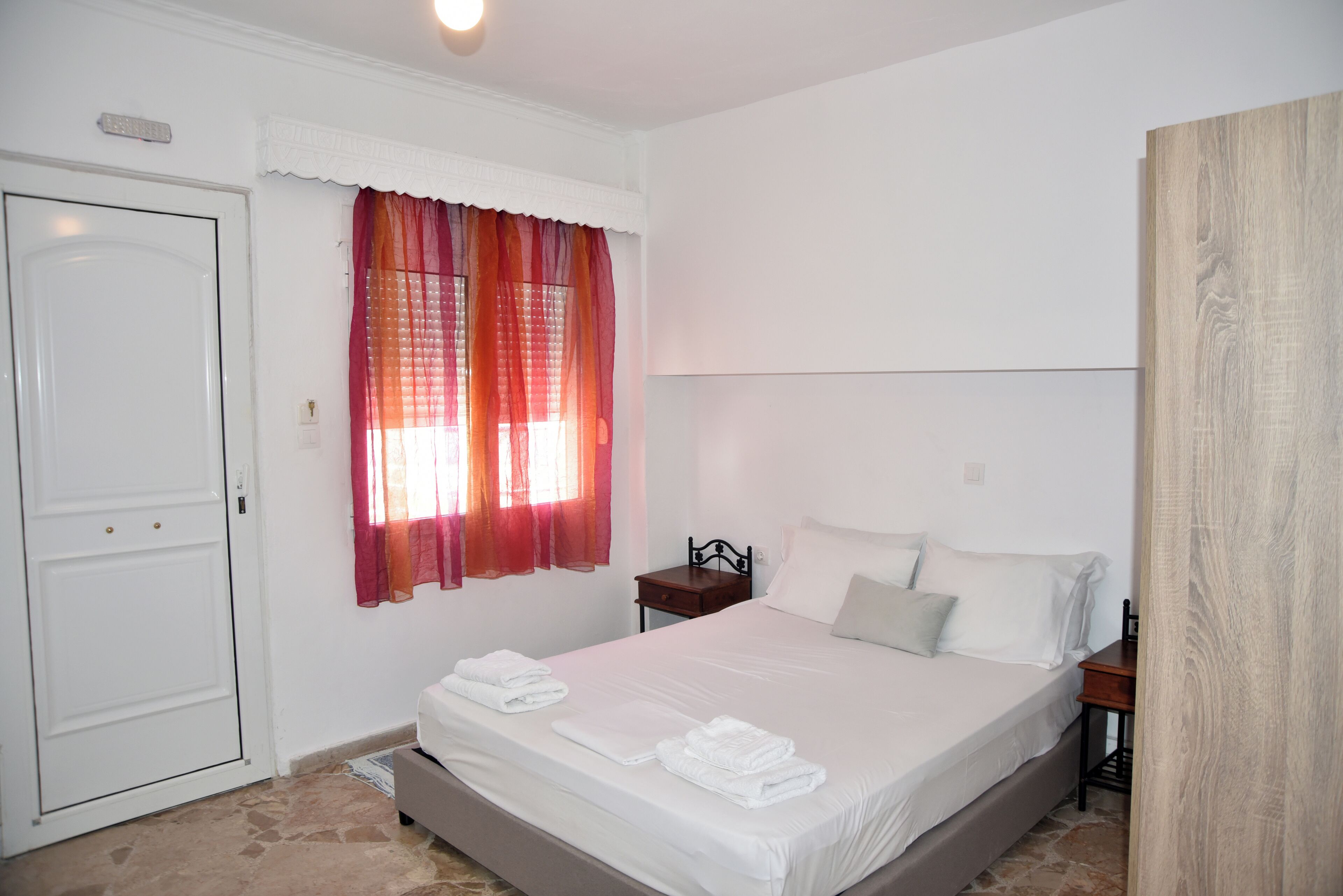 A bedroom with a bed, a nightstand, a door, and a window with curtains.