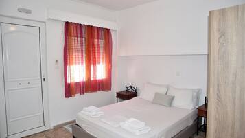 A bedroom with a bed, a nightstand, a door, and a window with curtains.