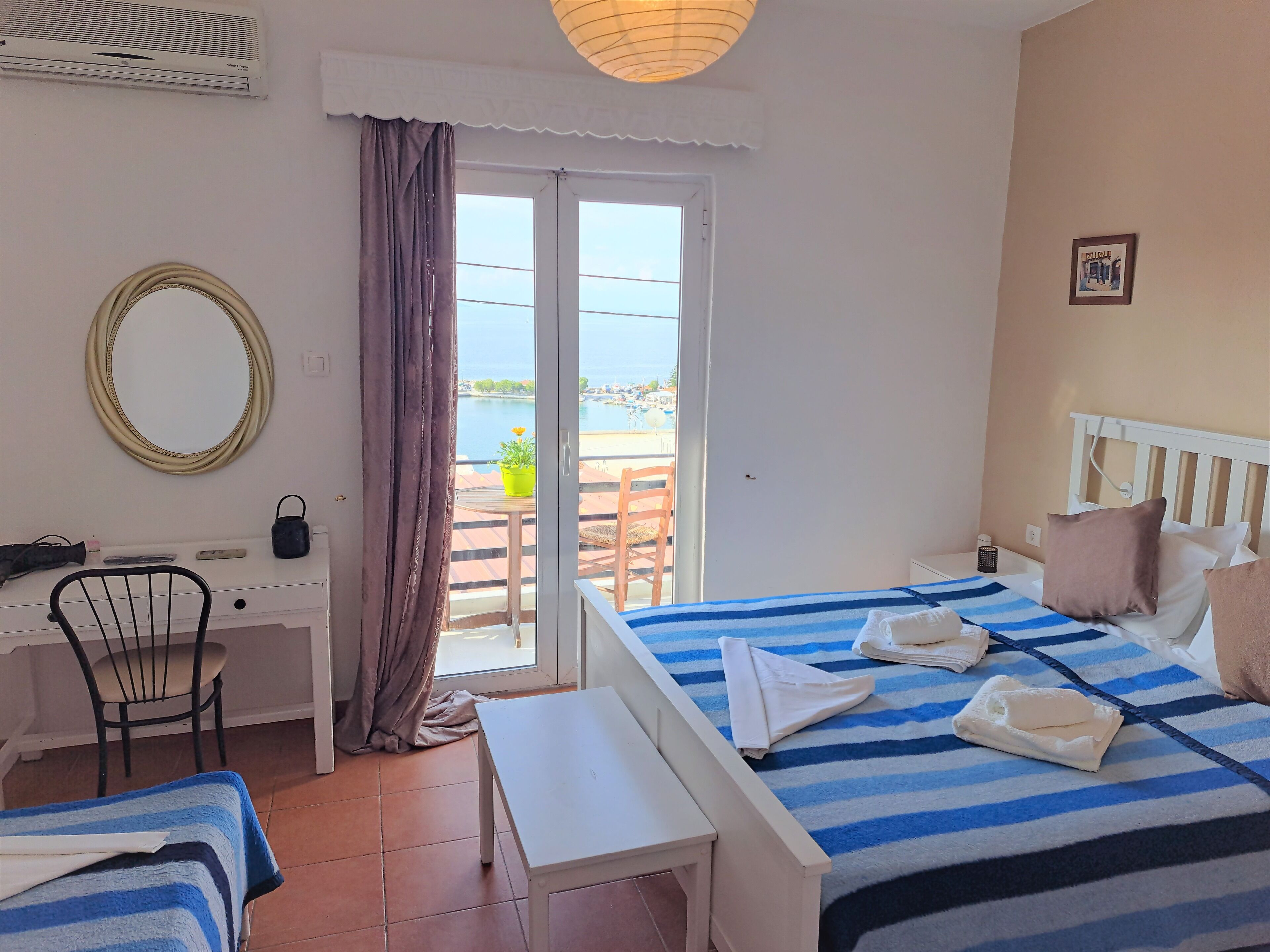 A hotel room with a bed, a desk, a chair, a small table, and a view of the sea through a glass door.