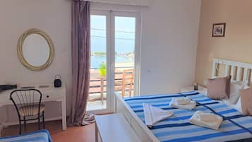 A hotel room with a bed, a desk, a chair, a small table, and a view of the sea through a glass door.