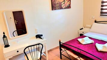 Habitación de hotel con cama, escritorio con silla, espejo, mesita de noche y una obra de arte colgada en la pared.