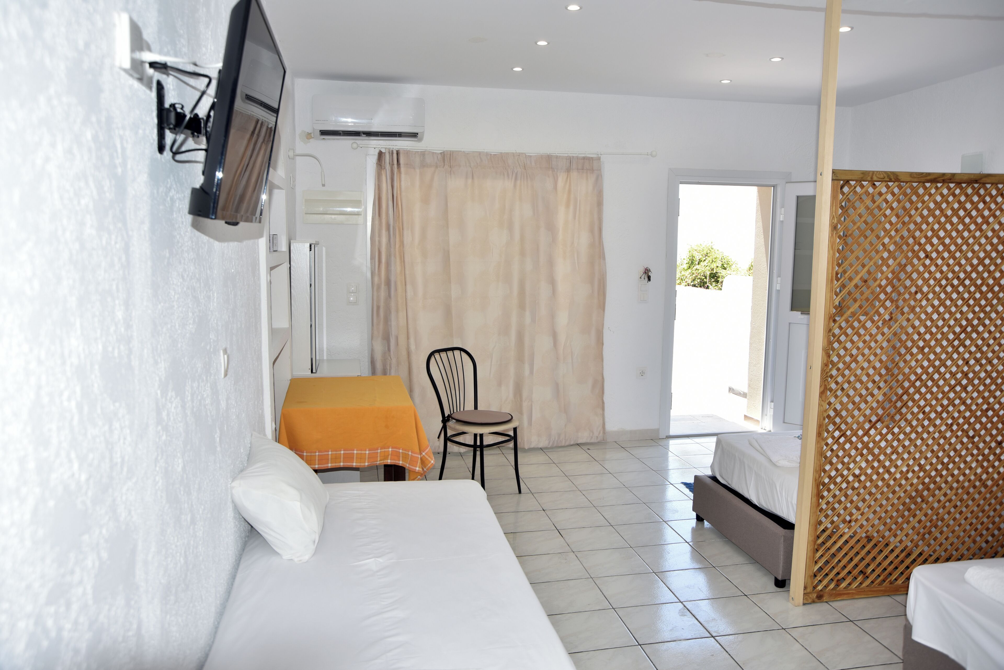 Une chambre d’hôtel avec un lit, une petite table et une chaise, un téléviseur fixé au mur et une fenêtre avec des rideaux.