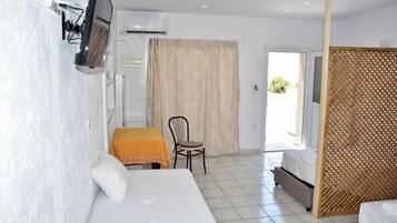 Une chambre d’hôtel avec un lit, une petite table et une chaise, un téléviseur fixé au mur et une fenêtre avec des rideaux.