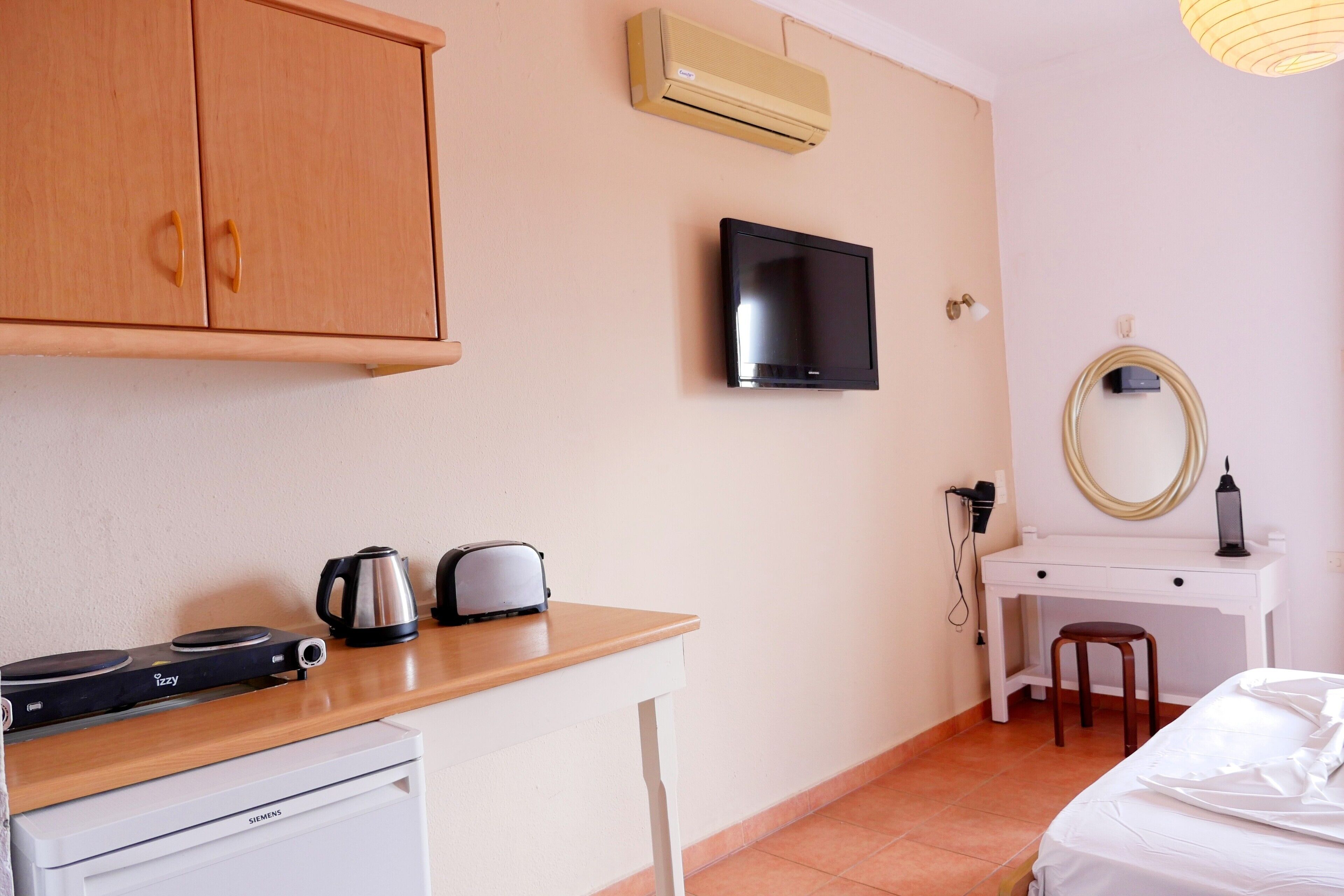 Ett kompakt hotellrum med ett litet pentry, en platt-TV, ett skrivbord med en stol, en säng och en spegel.