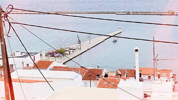 Une ville côtière dotée d’une jetée qui s’avance dans la mer, entourée de bâtiments aux toits recouverts de tuiles rouges.