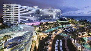Um hotel grande com vários andares, área de piscina e espaço ao ar livre bem iluminado com cadeiras de lounge.