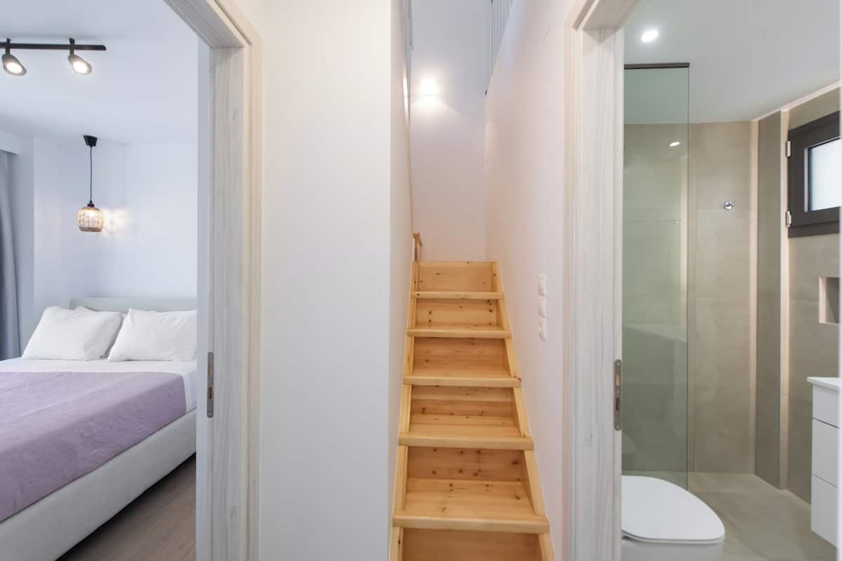 A bedroom with a bed, a wooden staircase, and a bathroom with a toilet and shower.