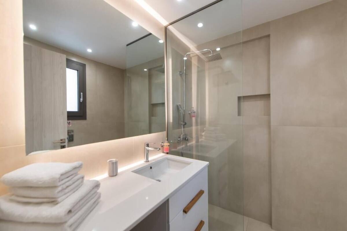 A modern bathroom with a glass-enclosed shower, a white sink with a mirror above it, and a stack of white towels on the counter.