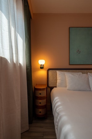 A hotel room with a bed, a nightstand with a lamp, a small round table, and a painting on the wall. - Coastal Condo with Side Ocean View Balcony (Belleair Beach)