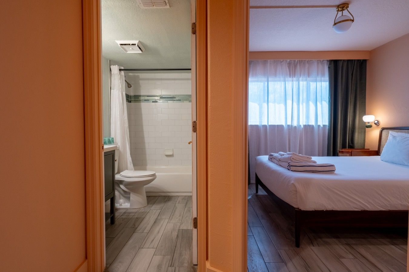 A hotel room with a shower, toilet, and a bed with towels.