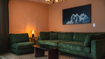 A living room with a sectional sofa, a coffee table, a lamp, and a painting of clouds on the wall.