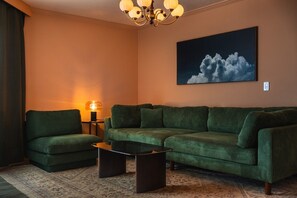 A living room with a sectional sofa, a coffee table, a lamp, and a painting of clouds on the wall. - Coastal Condo with Side Ocean View Balcony (Belleair Beach)