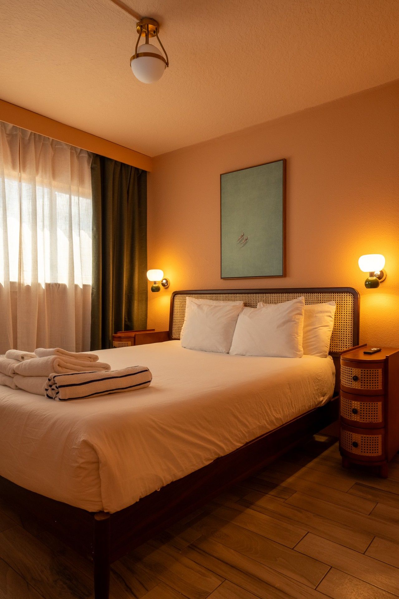 A hotel room with a bed, a nightstand, a wall-mounted lamp, and a painting.