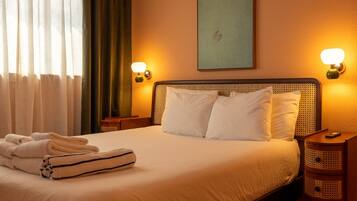 A hotel room with a bed, a nightstand, a wall-mounted lamp, and a painting.