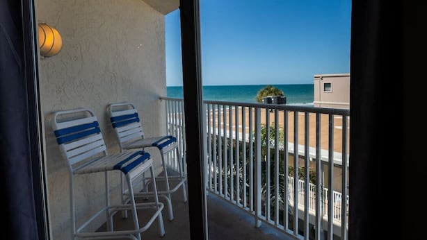 A balcony with two white chairs with blue stripes, a potted plant, and a view of the beach and ocean.