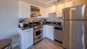 A compact kitchen with white cabinets, a stainless steel refrigerator, a built-in oven, a microwave, and a coffee maker.
