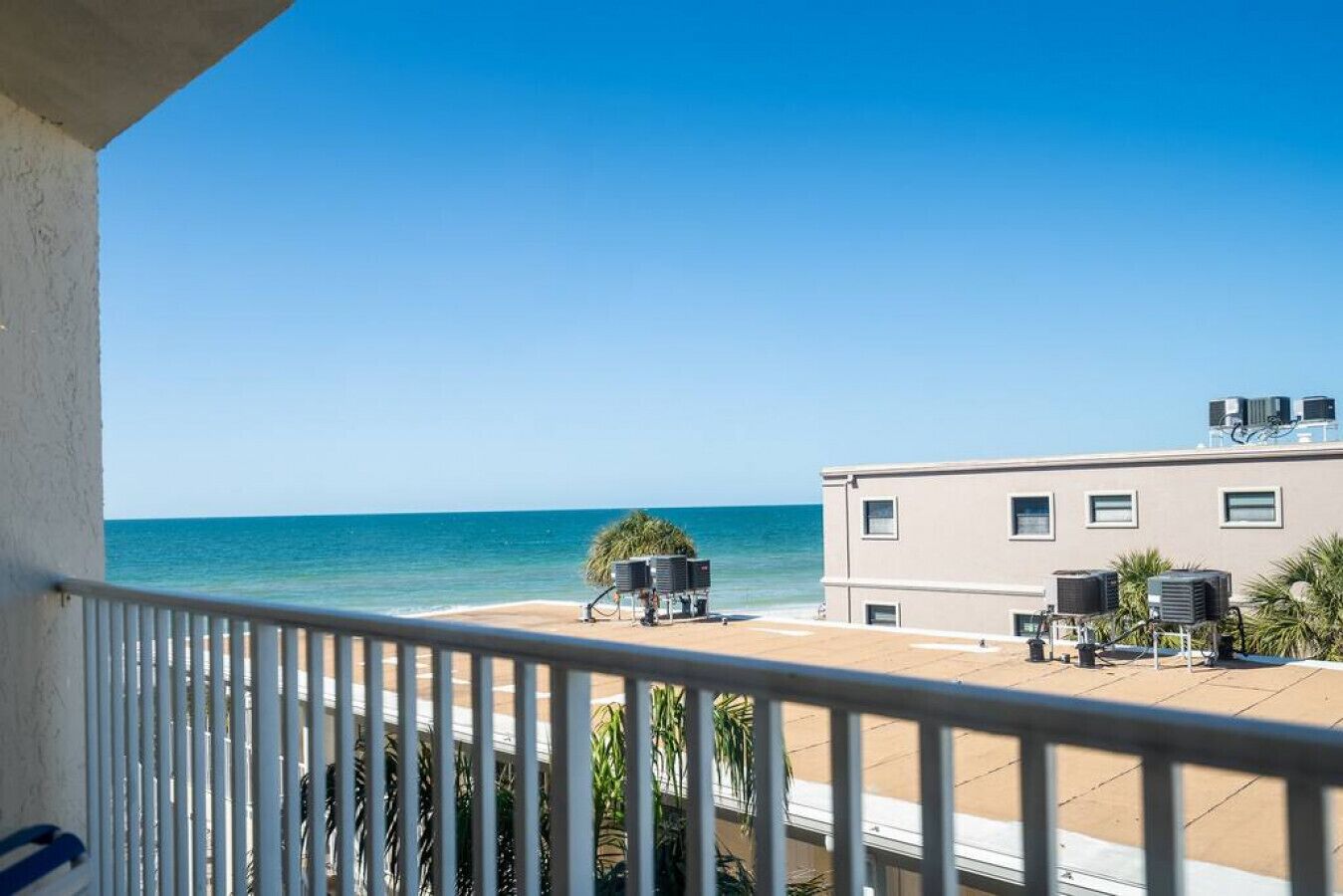 Een balkon met uitzicht op zee, een gebouw met airconditioners en een palmboom.