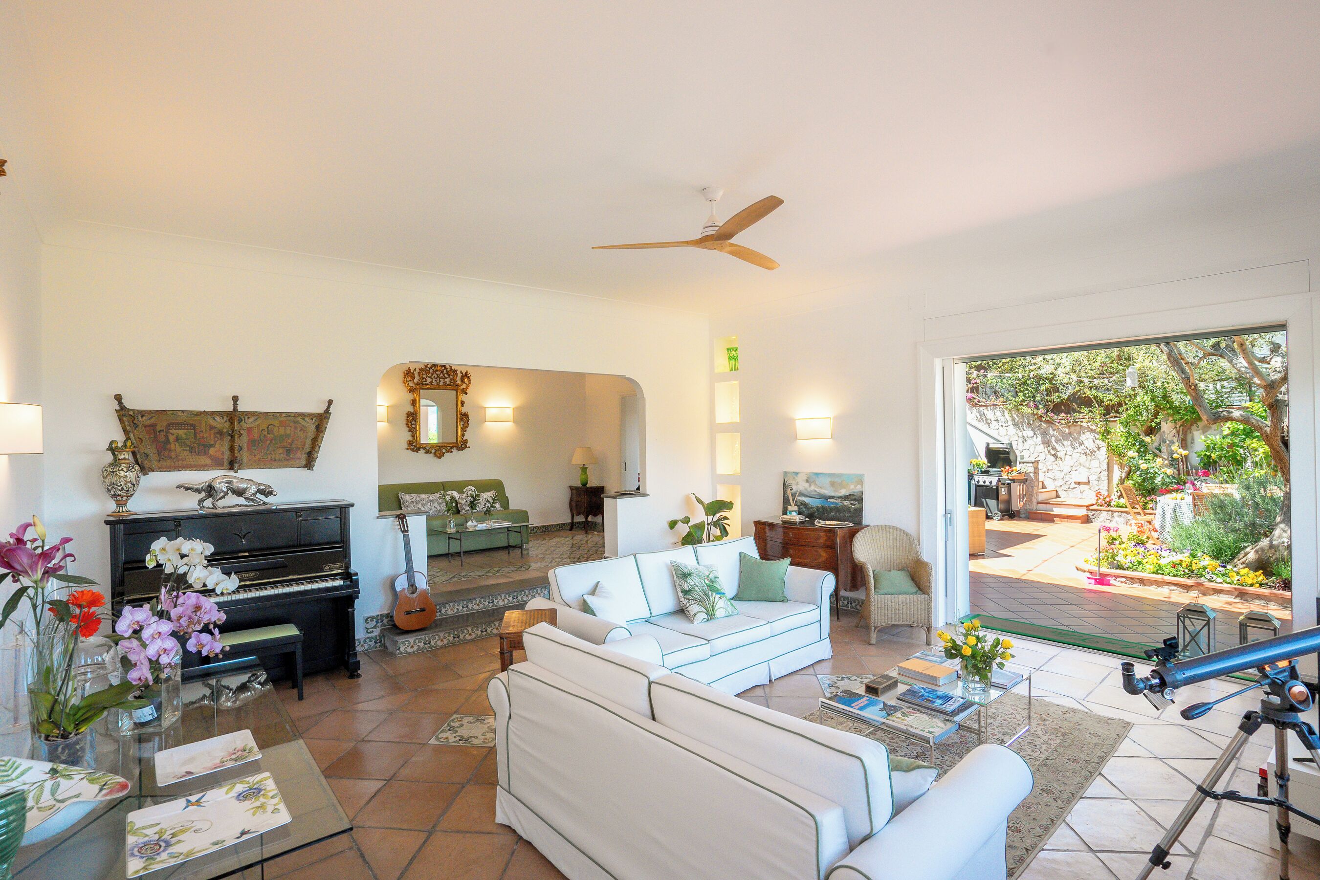 A spacious living room with a piano, a white sofa, a glass coffee table, and a telescope.