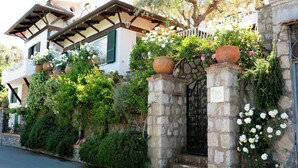 Una villa con ingresso in pietra, verde lussureggiante e un balcone con piante in vaso.