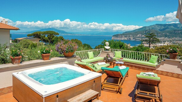 Una terrazza sul tetto con vasca idromassaggio, sedute imbottite verdi e una vista panoramica sull'oceano.