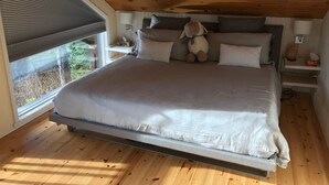 A bedroom with a bed, pillows, a stuffed toy, a window, and a wooden ceiling.