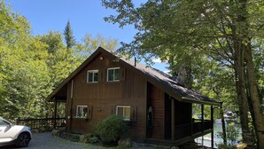 A wooden cabin with a porch, a covered deck, and a view of a lake.