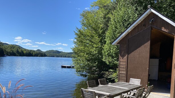 A wooden deck with a table and chairs overlooking a lake, a shed, and a dock.