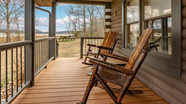 En træterrasse med to gyngestole og et picnicbord, med udsigt over et naturligt landskab.