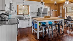 Et køkken med hvide skabe, træloft og en central ø med barstole.