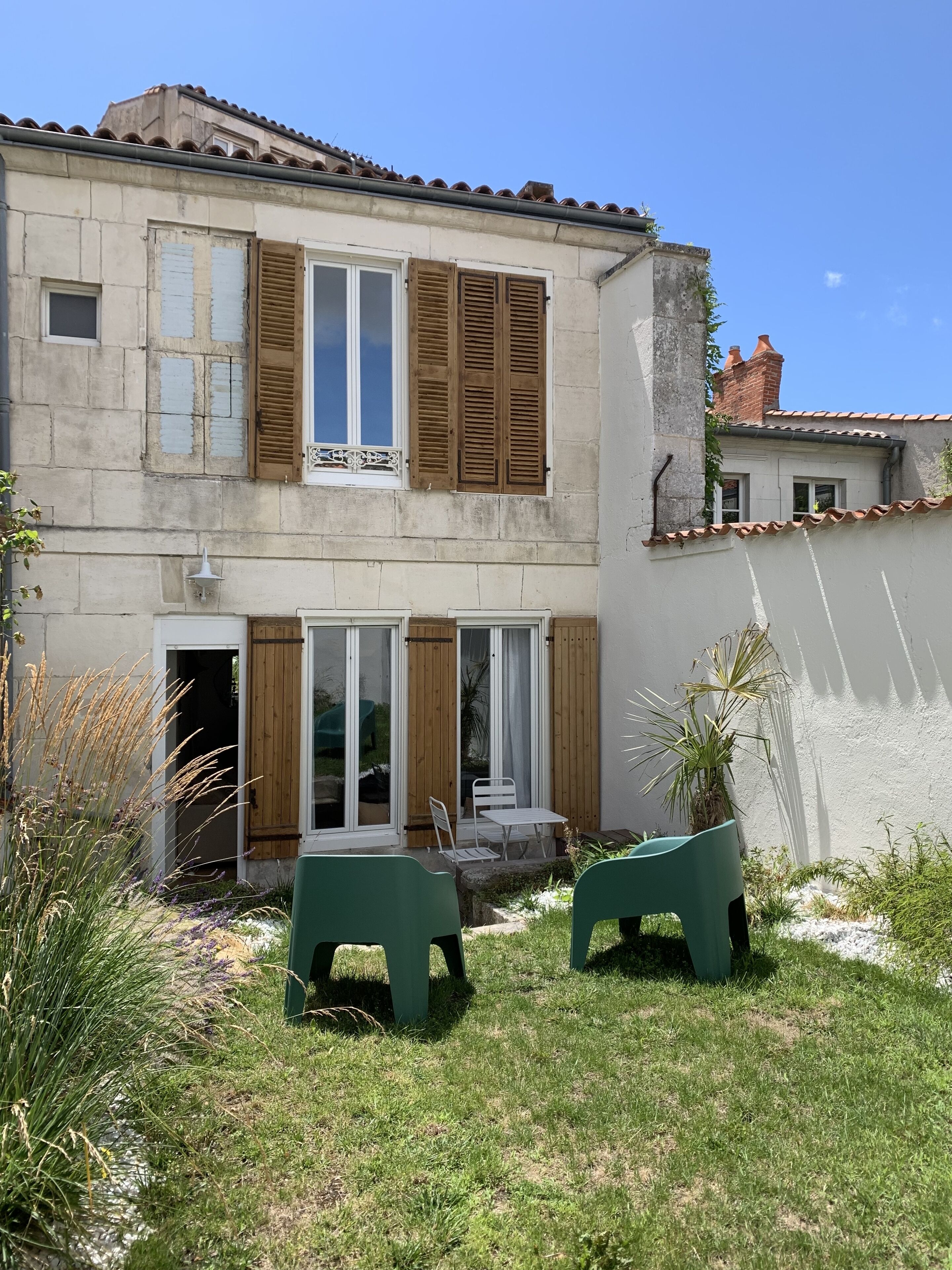 A two-story house with a garden patio, wooden shutters, and a white exterior.