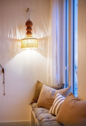 A cozy room with a hanging lamp, a window with curtains, and a bench with cushions.