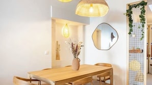 Ein Essbereich mit einem Holztisch und Stühlen, Pendelleuchten, einer Vase mit Blumen, einem Spiegel und einer Wand mit Rastermuster und Grünpflanzen.