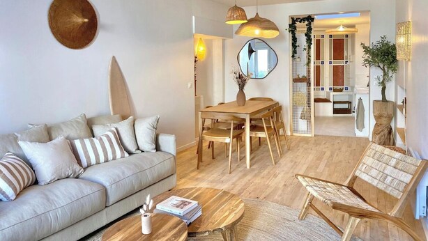 Ein modernes Wohnzimmer mit Sofa, Couchtisch und Esstisch. An der Wand hängt ein Spiegel und in der Ecke steht eine Pflanze.