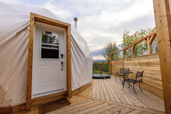 A covered wooden deck with a white door, a small table, and two chairs.