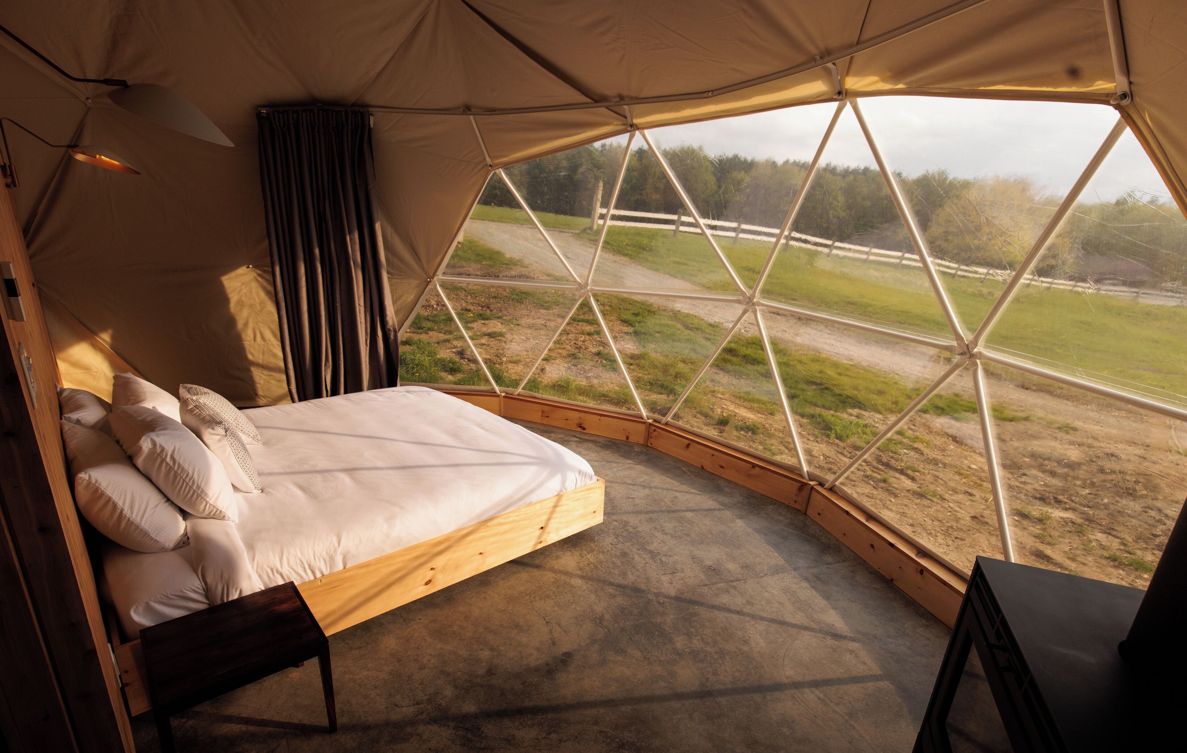 A tented room with a bed, a wooden bench, and a view of a rural landscape.