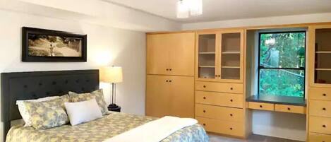 A bedroom with a bed, a nightstand, a lamp, a wardrobe, and a window with a view of greenery.